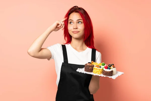 Chef Pastelaria Segurando Muffins Isolados Fundo Rosa Com Dúvidas Pensamento — Fotografia de Stock