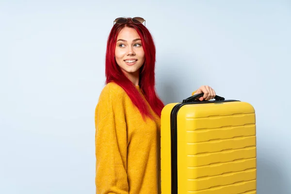 抱着一个蓝色背景的手提箱的旅行女孩 双臂交叉 快乐极了 — 图库照片