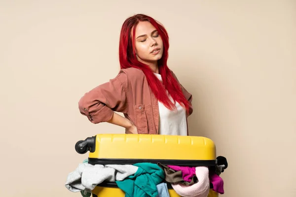 旅行的女孩 提着一个装满衣服的手提箱 衣服因米黄色背景而被隔离 背痛难忍 — 图库照片