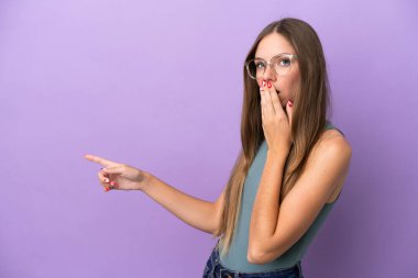 Genç Litvanyalı kadın, mor arka planda izole edilmiş, sürpriz bir ifadeyle işaret ederken...