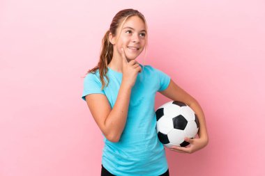 Little football player girl isolated on pink background thinking an idea while looking up
