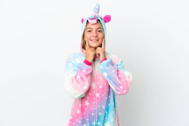 Beyaz arka planda izole edilmiş tek boynuzlu at pijamalarıyla mutlu ve hoş bir ifadeyle gülümseyen küçük kız.