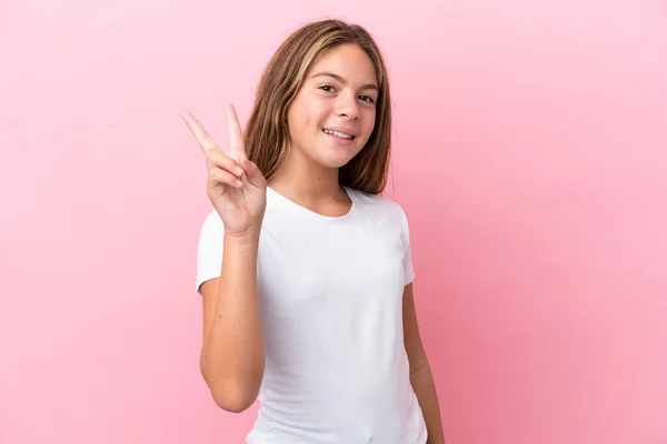 一个被粉色背景隔离的高加索小女孩笑着展示胜利的标志 — 图库照片