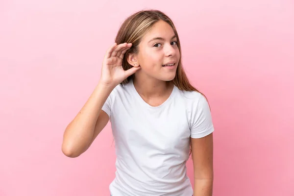 ピンクの背景に孤立した小さな白人の女の子は耳に手を置くことによって何かを聞いて — ストック写真