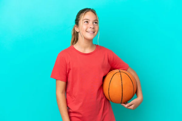 青い背景に孤立したバスケットボールをしている小さな白人の女の子考えを考えながら見上げます — ストック写真
