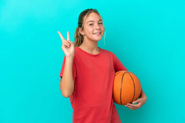 파란색 배경에서 고립된 농구를 코카서스 소녀가 웃으며 승리의 표시를 — 스톡 사진