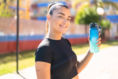 Genç, güzel, esmer bir kadın, elinde bir şişe su var.