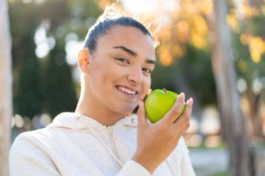 Genç, güzel, spor bir kadın elinde mutlu bir ifadeyle bir elma tutuyor.