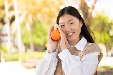 Açık havada elinde portakal tutan güzel bir Çinli kadın.