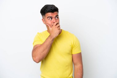 Beyaz arka planda soyutlanmış beyaz tenli yakışıklı bir genç. Şüpheleri var ve kafası karışmış bir yüz ifadesi var.