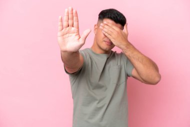 Pembe arka planda izole edilmiş beyaz tenli yakışıklı adam jesti durdurup yüzünü kapatıyor.