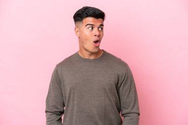 Pembe arka planda izole edilmiş beyaz, yakışıklı genç bir adam yan tarafa bakarken sürpriz jest yapıyor.