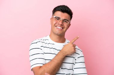 Pembe arka planda gözlüklü ve işaret eden beyaz tenli yakışıklı bir adam.