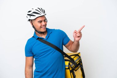 Beyaz arka planda izole edilmiş termal sırt çantalı beyaz tenli genç beyaz bir adam parmak göstererek bir ürün sunuyor.