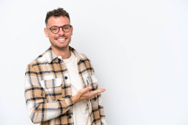 Beyaz arka planda izole edilmiş beyaz tenli yakışıklı genç bir adam bir fikir sunuyor ve gülümsüyor.
