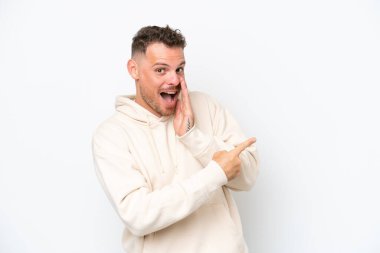 Beyaz arka planda soyutlanmış beyaz tenli yakışıklı bir adam bir ürün sunmak ve bir şeyler fısıldamak için kenarı işaret ediyor.