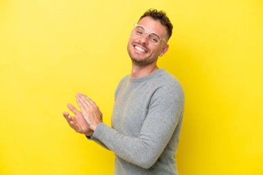 Sarı arka planda izole edilmiş beyaz, yakışıklı bir adam alkışlıyor.