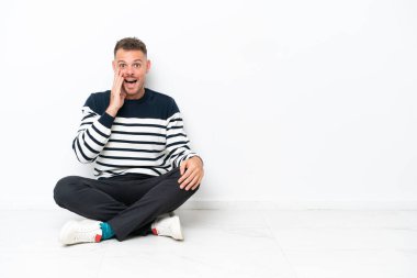 Young man sitting on the floor isolated on white background with surprise and shocked facial expression