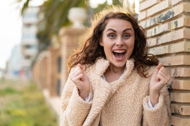 Açık havada genç beyaz kadın galibiyet pozisyonunu kutluyor.