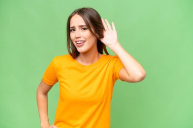 Young pretty caucasian woman over isolated background listening to something by putting hand on the ear