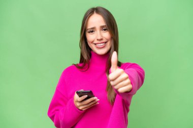 Young beautiful caucasian woman over isolated background using mobile phone while doing thumbs up