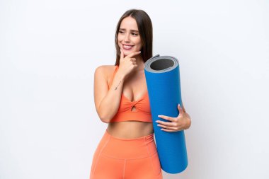 Young beautiful sport woman going to yoga classes while holding a mat isolated on white background looking to the side and smiling