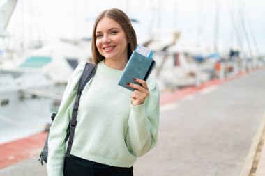 Sarışın, güzel bir kadın elinde pasaport tutarken gülümsüyor.