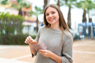 Genç, güzel, sarışın bir kadın. Cüzdanı elinde, mutlu bir ifadesi var.