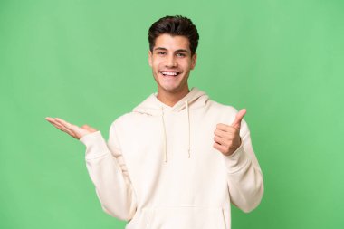 İzole edilmiş arka plan üzerinde genç beyaz yakışıklı bir adam. Avucunun içinde hayali bir şey tutuyor. Bir ilan vermek için.