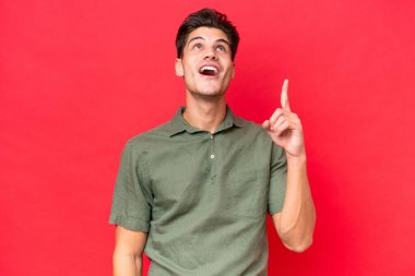 Kafkasyalı yakışıklı adam kırmızı arka planda izole edilmiş yukarı bakıyor ve şaşırıyor.