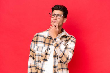 Genç beyaz yakışıklı adam kırmızı arka planda izole edilmiş ve yukarı bakıyor.