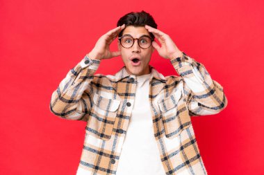 Kafkasyalı yakışıklı genç adam, kırmızı arka planda izole edilmiş, sürpriz bir ifadeyle.