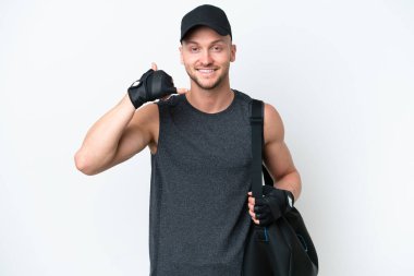 İzole edilmiş beyaz arka planda spor çantalı, genç sarışın, beyaz bir adam telefon jesti yapıyor. Bana geri dönüş işareti ver.