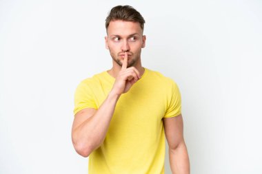 Beyaz arka planda izole edilmiş genç sarışın beyaz adam sessiz bir jest işareti gösteriyor. Parmağını ağzına sokuyor.