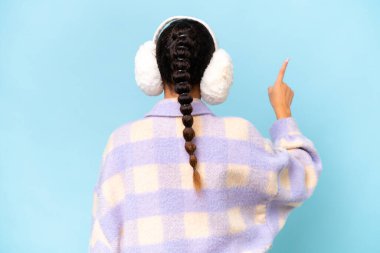 Mavi arka planda izole edilmiş kışlık manşet giyen genç bir Arap kadını işaret parmağıyla işaret ediyor.