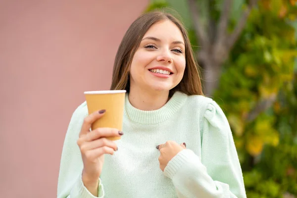 年轻漂亮的金发女子在户外端着咖啡 脸上带着惊讶的表情 — 图库照片