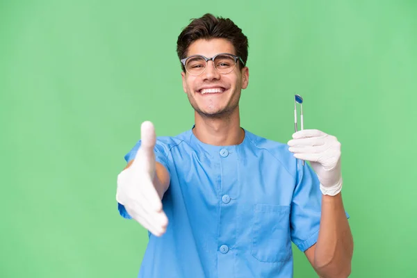Jovem Dentista Homem Segurando Ferramentas Sobre Fundo Isolado Apertando Mãos — Fotografia de Stock