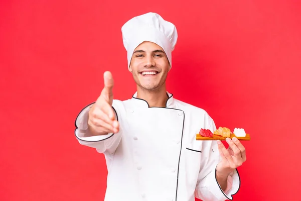Joven Chef Caucásico Sosteniendo Sashimi Aislado Sobre Fondo Rojo Estrechando — Foto de Stock