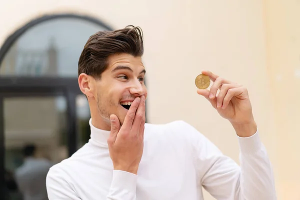 stock image Young caucasian man holding a Bitcoin at outdoors with surprise and shocked facial expression