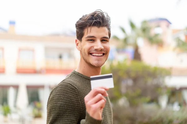 Młody Biały Mężczyzna Trzymając Kartę Kredytową Zewnątrz Uśmiechając Się Dużo — Zdjęcie stockowe