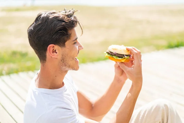 Młody Biały Człowiek Trzyma Hamburger Zewnątrz Szczęśliwy Ekspresja — Zdjęcie stockowe