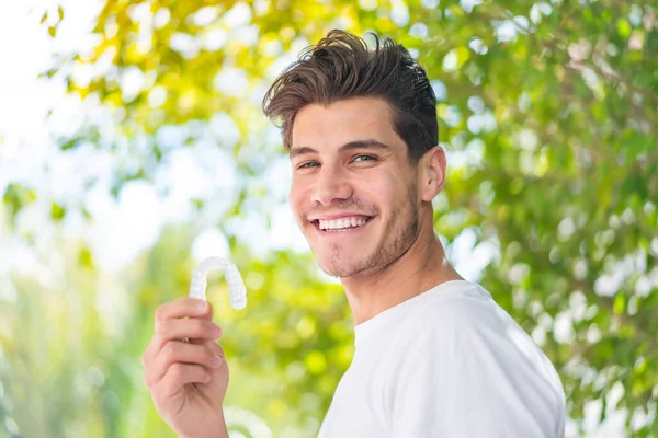 Young caucasian man holding invisible braces at outdoors smiling a lot