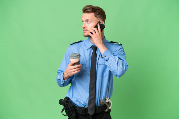 Young police man over isolated background holding coffee to take away and a mobile