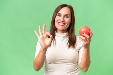 Stüdyonun arka planında elma tutan orta yaşlı kadın. 