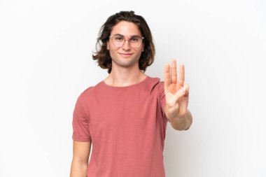 Beyaz arka planda izole edilmiş genç yakışıklı mutlu ve parmaklarıyla üçe kadar sayıyor.