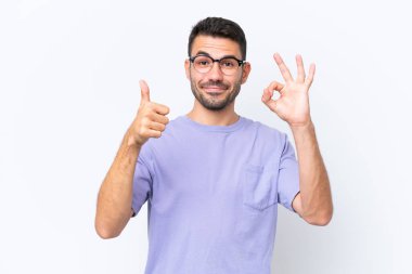Beyaz arka planda izole edilmiş genç beyaz bir adam Tamam işareti ve baş parmak işareti