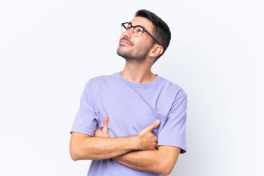 Beyaz arka planda izole edilmiş genç beyaz adam gülümserken yukarı bakıyor.