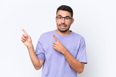 Beyaz arka planda izole edilmiş genç beyaz adam korkmuş ve kenarı işaret ediyor.