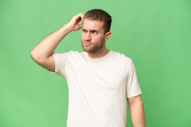 Genç, beyaz, yeşil krom arka planda izole edilmiş, kafası kaşınırken şüpheleri olan yakışıklı bir adam.