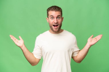 Yeşil krom arka planda izole edilmiş yakışıklı beyaz adam, şok olmuş yüz ifadesi.
